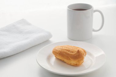 Kremalı pasta arka planda bir bardak ile beyaz bir tabakta uzanıyor. Işık anahtarında fotoğrafçılık