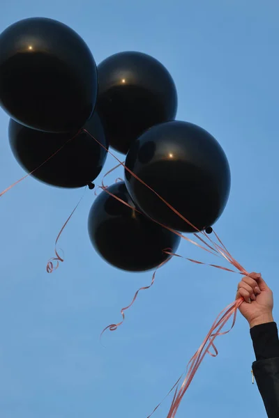 Woman\'s hand with black balloons against the blue sky. Black Fridays