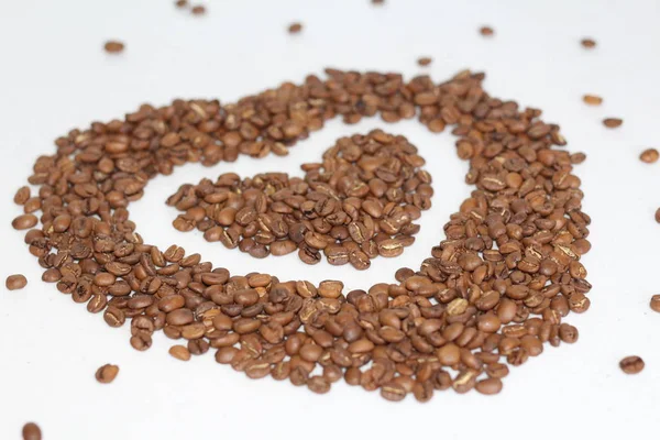 Heart of coffee beans. Coffee grains are scattered on a white table in the shape of a heart.