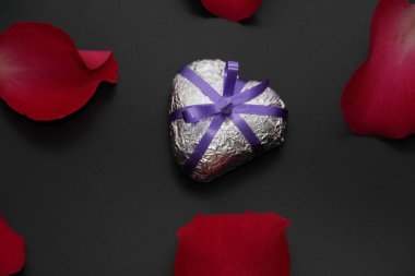 Metal kalp gül tarafından çevrili. Gümüş kalp kurdele ile süslenmiş. Kalp ve gül karanlık bir arka plan üzerinde.