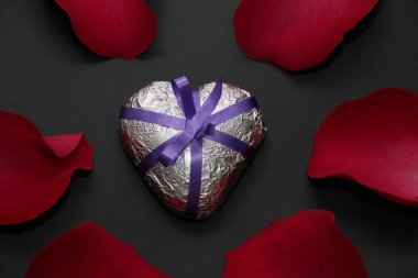 Metal kalp gül tarafından çevrili. Gümüş kalp kurdele ile süslenmiş. Kalp ve gül karanlık bir arka plan üzerinde.