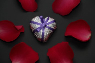 Metal kalp gül tarafından çevrili. Gümüş kalp kurdele ile süslenmiş. Kalp ve gül karanlık bir arka plan üzerinde.