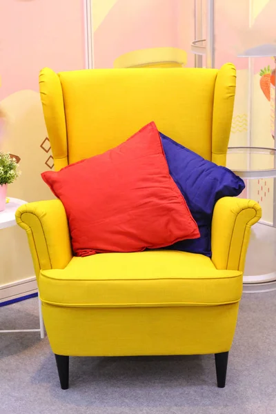 In the center is a bright yellow armchair, with two pillows on it - red and blue. No one in the photo. Armchair without people.
