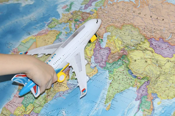 The toy plane flies by the geographical map. The plane is held by a child. The liner in his hand flies over the world map. Travel by plane.