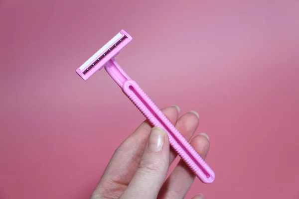 Pink razor in a beautiful female hand. Pink background. — Stock Photo, Image