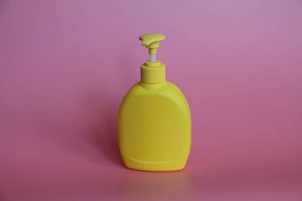 Botella de plástico amarillo sobre fondo rosa. Frasco amarillo con dispensador . — Foto de Stock