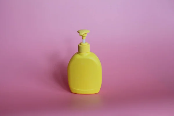 Botella de plástico amarillo sobre fondo rosa. Frasco amarillo con dispensador . — Foto de Stock