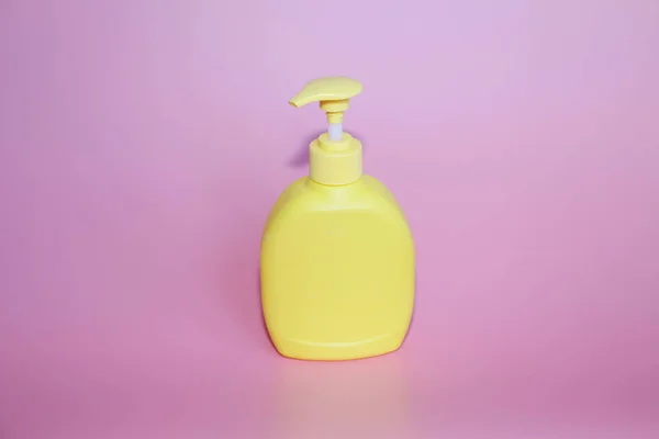 Жовта пластикова пляшка на рожевому тлі. Жовта пляшка з дозатором . — стокове фото
