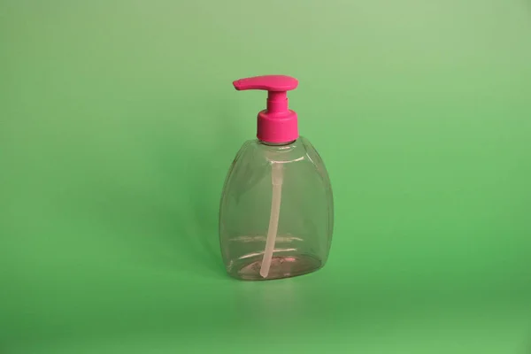 One red plastic bottle on a green background. Bottle for cosmetics with dispenser.