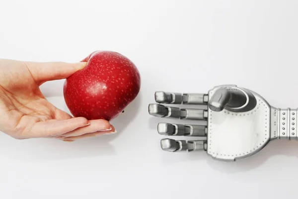 The hand of a real man gives the robot a red apple.