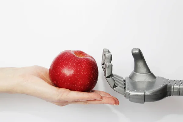 The hand of a real man gives the robot a red apple.