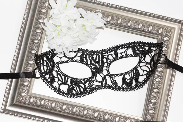 Black lace eye mask, vintage frame and white flowers. — Stock Photo, Image