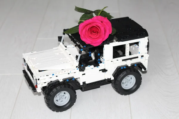 O carro de brinquedo SUV carrega uma verdadeira rosa vermelha . — Fotografia de Stock
