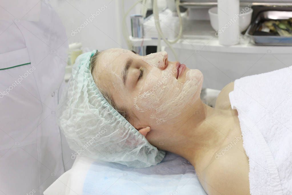 In the beauty salon a young woman is doing a peeling on her face.