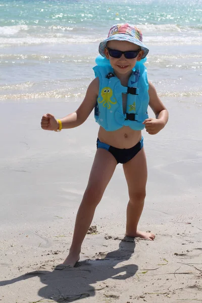 Piccolo ragazzo carino sulla spiaggia in un giubbotto di salvataggio . — Foto Stock