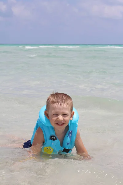 Piccolo ragazzo carino sulla spiaggia in un giubbotto di salvataggio . — Foto Stock