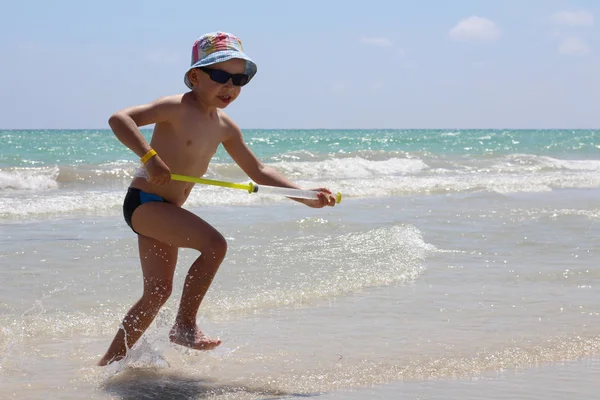 Un piccolo ragazzo carino corre lungo la spiaggia e gioca . — Foto Stock