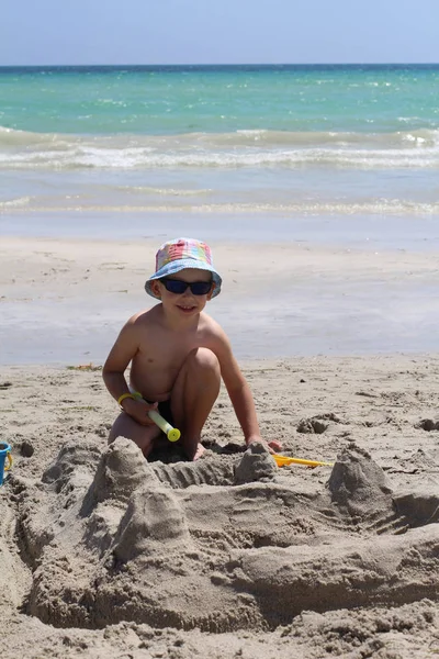 Piccolo ragazzo carino costruisce un castello di sabbia. Casa di sabbia sulla spiaggia . — Foto Stock