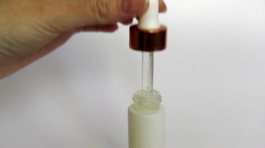 Bir kadın elinde gualinik sıvı ile Pipet. Beyaz bir şişeye damlayan bir damla. Cilt için altın parçacıkları ile serum. Sıvı altın parçacıkları ile cildi nemlendirin. 