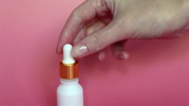 Bir kadın elinde gualinik sıvı ile Pipet. Beyaz bir şişeye damlayan bir damla. Cilt için altın parçacıkları ile serum. Sıvı altın parçacıkları ile cildi nemlendirin. 