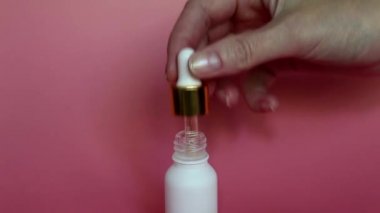 Bir kadın elinde gualinik sıvı ile Pipet. Beyaz bir şişeye damlayan bir damla. Cilt için altın parçacıkları ile serum. Sıvı altın parçacıkları ile cildi nemlendirin. 