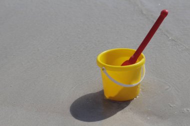 Sarı bir bebek kovası ve denizde kum üzerinde kırmızı bir kürek standı.