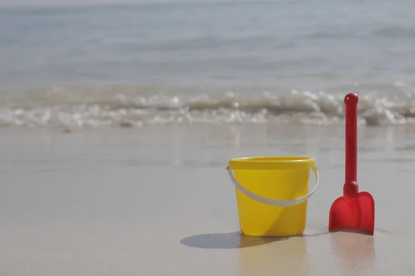 Желтое ведро для младенцев и красная лопата стоят на песке у моря . — стоковое фото