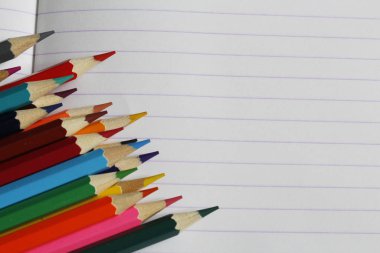 Renkli kalemler çizgili bir defterüzerinde yatıyor. Metin için bir yer var.