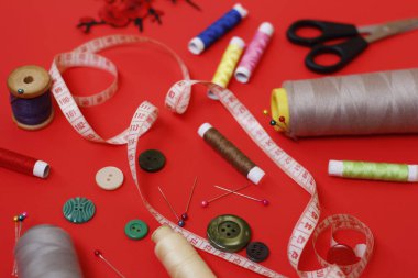 Kırmızı arka plan üzerinde dikiş iplikleri ve dikiş aksesuarları ile kompozisyon.