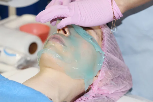 Um salão de beleza, um cosmetologista remove o pó de uma máscara facial de descascamento de alginato . — Fotografia de Stock