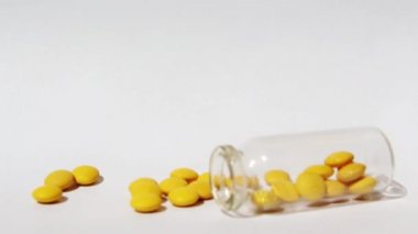 Sarı haplar şeffaf cam bir kavanozdan düşer. Kadın elinde cam kavanoz. Sarı haplar beyaz arka planda yatıyor.. 