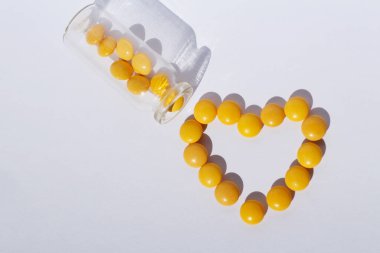 Sarı tabletlerden kalbi çıkardı. Tıbbi tema. Konsept kalp için vitaminler. Haplar şişeden düşer..