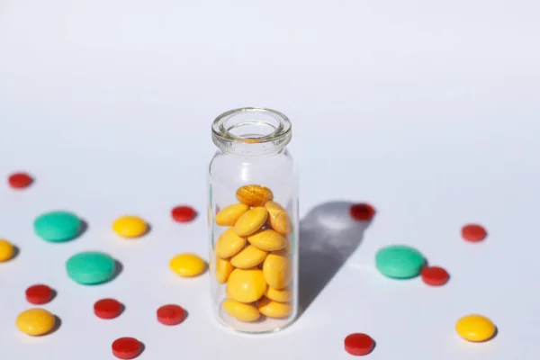 A glass container with prescription medicine is standing, and multi-colored tablets are scattered nearby. Medical theme.