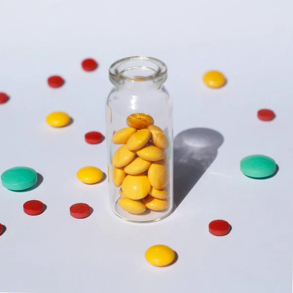 A glass container with prescription medicine is standing, and multi-colored tablets are scattered nearby. Medical theme.