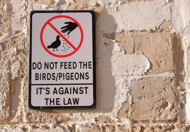 Uyarı levhası diyor ki - güvercinleri / kuşları beslemeyin - yaşlı kum taşından duvara yerleştirilmiş. Resimli uyarı levhası Valletta, Malta sokaklarındaki kuralları açıklıyor