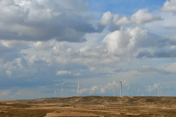 Dramatic cumulus rain clouds cover dry agricultural land in Teruel region, Spain. Wind energy generating turbines visible on horizon. Conceptual for climate change, global warming