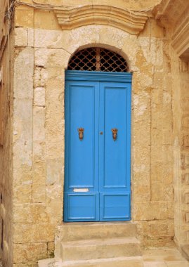 Birgu, Malta 'da merdivenleri olan kum rengi duvarda klasik tarz mavi renkli çift kapı. Dairenin kapali yasli girisi, ustunde metal süslemeler varmis.