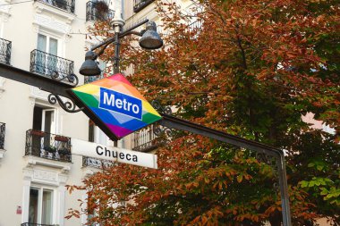 Chueca metro station signboard with autumnal background outside in Madrid, Spain. Subway entrance with lgbt symbolic in gay district. clipart