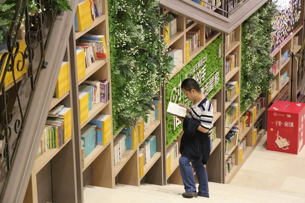 2018年10月9日 重庆一家购物中心 一名顾客在由数千本书上架形成的10米高的书墙前看书 — 图库照片