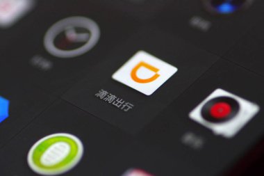 A Chinese mobile phone user looks at the icon of the mobile app of taxi-hailing and car service Didi Chuxing on his smartphone in Ji'nan city, east China's Shandong, 29 August 2018 clipart