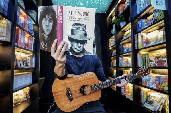 成都厳寺を書店のスタッフ メンバーのカナダのシンガー ソング ライター ニール ヤングの音楽家の肖像画を 読み取りになりたい つになる を提唱する表紙の本と強制遠近法写真のポーズ を予熱するには — ストック写真