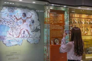 A passenger takes photos of a reproduction of a mural from the tomb chapel of Nebanum, Thebes, Egypt, showing Nebamun hunting birds in the marshes around the Nile, from the British Museum's collection on display at the South Shaanxi Road Metro statio clipart
