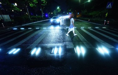 A pedestrian walks on an intelligent zebra crossing as the lights controlled by a motion sensor are triggered and turn on in Hangzhou city, east China's Zhejiang province, 2 July 2018 clipart