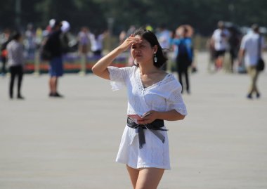 A tourist tries to shield herself with one of her hands from the scorching sun as she visits the Tian'anmen Square in Beijing, China, 31 May 2018 clipart