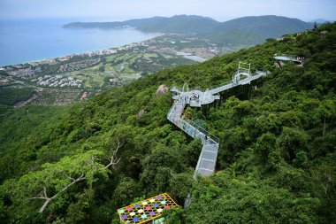 Tourists walk on a glass-bottomed sky walkway at the Yalong Bay forest park in Sanya city, south China's Hainan province, 29 July 2018 clipart