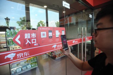 A customer uses his smartphone to scan a QR code at an unmanned convenience store of online retailer JD.com in Wuhan city, central China's Hubei province, 15 June 2018 clipart