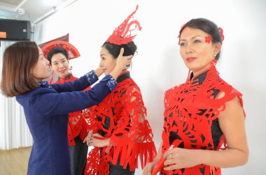 36-year-old Chinese craftsman Liang Ying, an inheritor of paper-cuttings, help models wear head accessories, capes, and earrings made of paper-cutting created by herself before a show in Liaocheng city, east China's Shandong province, 4 February 2018 clipart