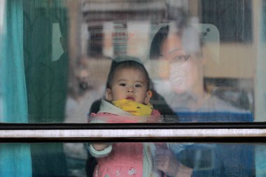 A mother and her child look outsde the window of a train as they are on their way back home for the upcoming Chinese Lunar New Year, also known as Spring Festival, at the Harbin Railway Station in Harbin city, northeast China's Heilongjiang province, clipart