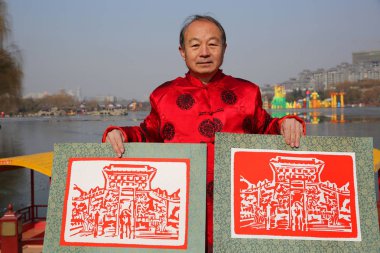 61-year-old craftman Lyv Guoling displays a pair of paper-cuttings showing snow scenery of a landmark tourist attraction in Xi'an city, northwest China's Shaanxi province, 6 February 2018 clipart
