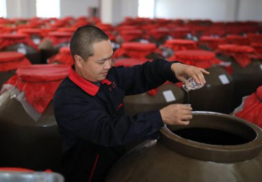 A Chinese worker checks Bijie Daqu, a sub-brand Chinese liquor derived from Moutai, which is a Chinese brand of baijiu liquor, in a jar at a production plant in Bijie city, southwest China's Guizhou province, 10 April 2018 clipart